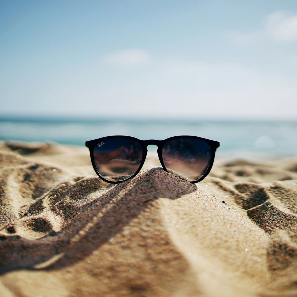 A pair of sunglasses on a sandy beach in front of a blue sky